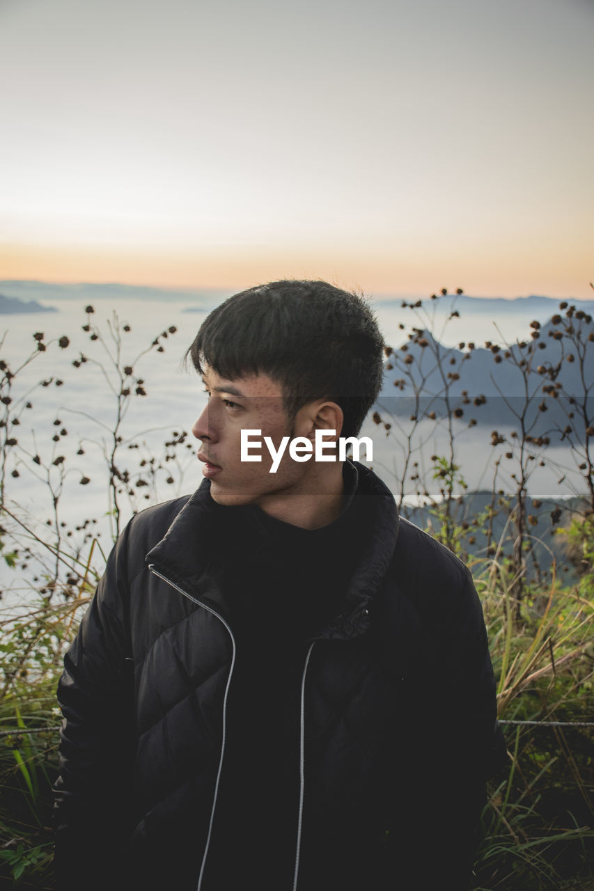 Young man looking away while standing on mountain peak