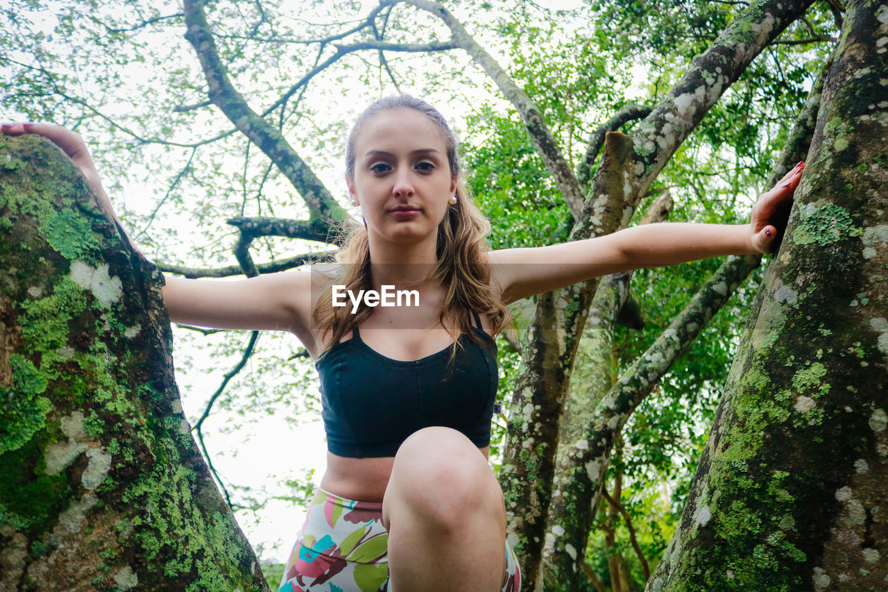 Low angle view of young woman sitting on tree at park