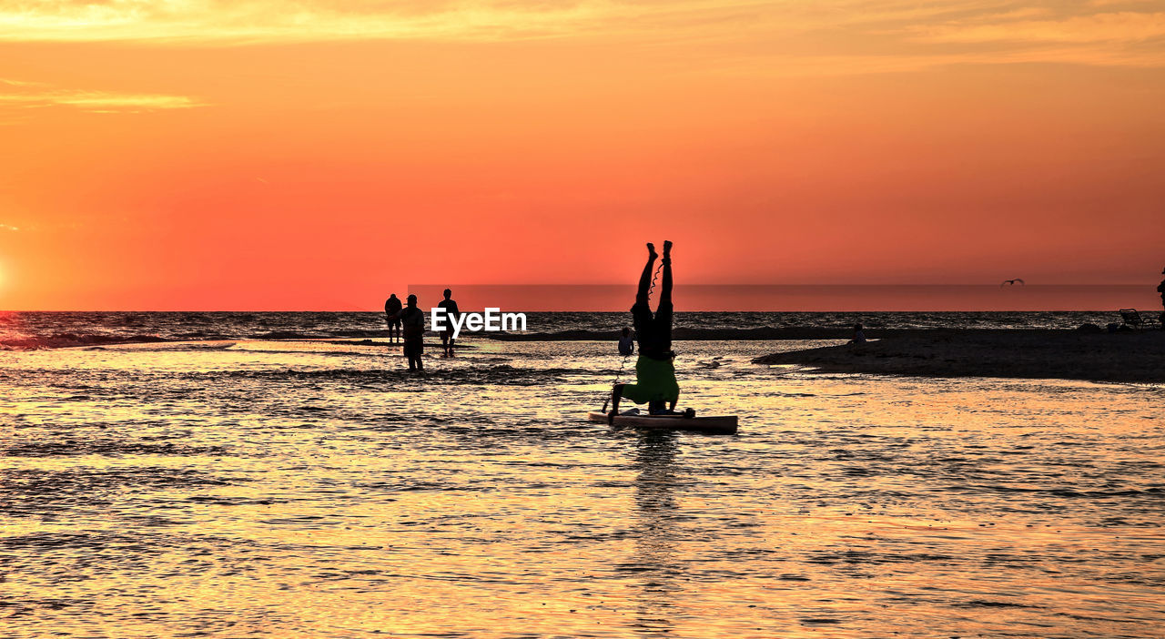 SILHOUETTE PEOPLE IN SEA AGAINST ORANGE SKY