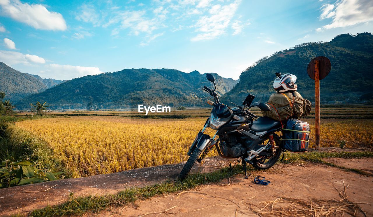 MOTORCYCLE ON ROAD BY FIELD AGAINST SKY