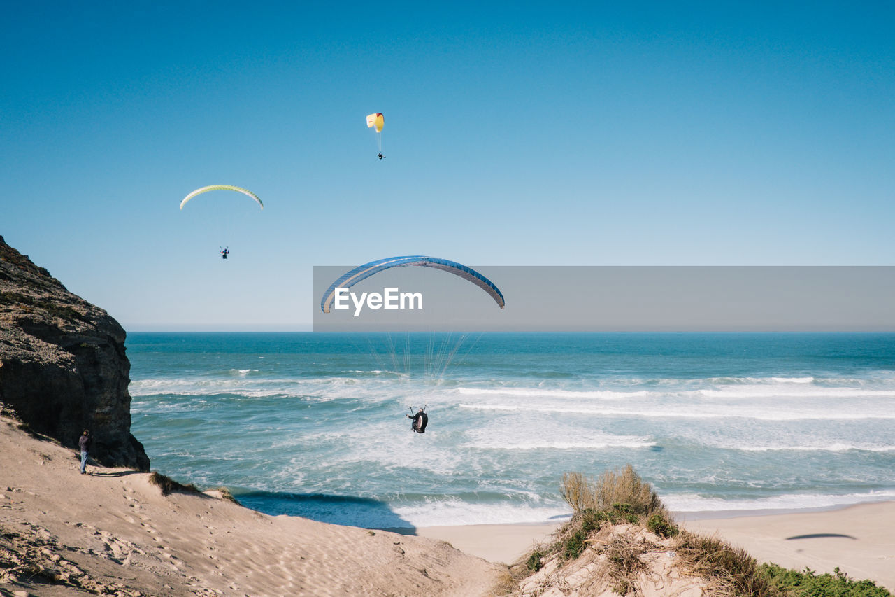 People paragliding over sea against clear blue sky
