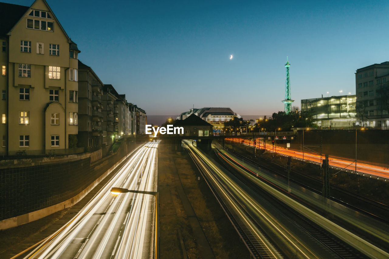 LIGHT TRAILS ON ILLUMINATED STREET AMIDST BUILDINGS IN CITY