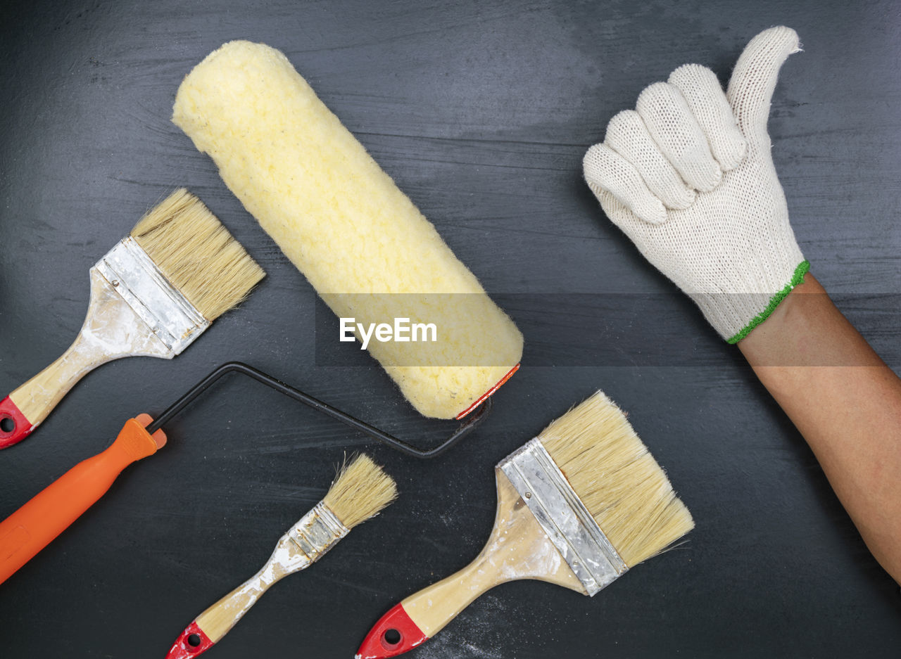 Hand with paintbrushes and roller on table