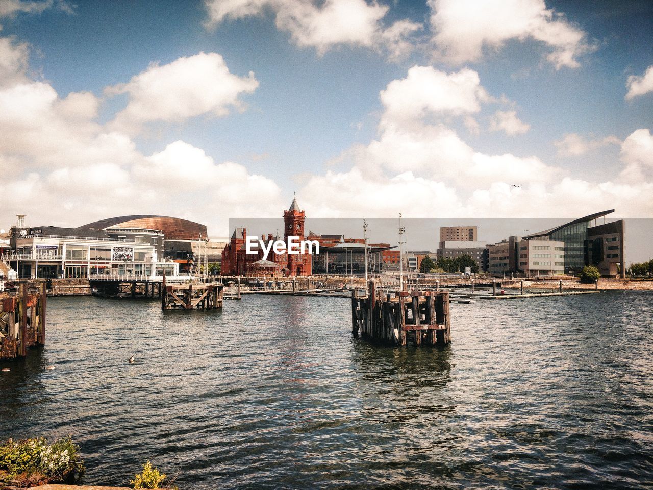 Buildings by river and sea against cloudy sky in city with vintage look and reflections