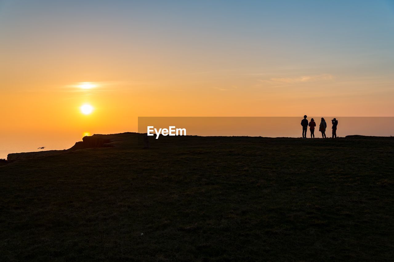 Silhouette men on landscape against sky during sunset