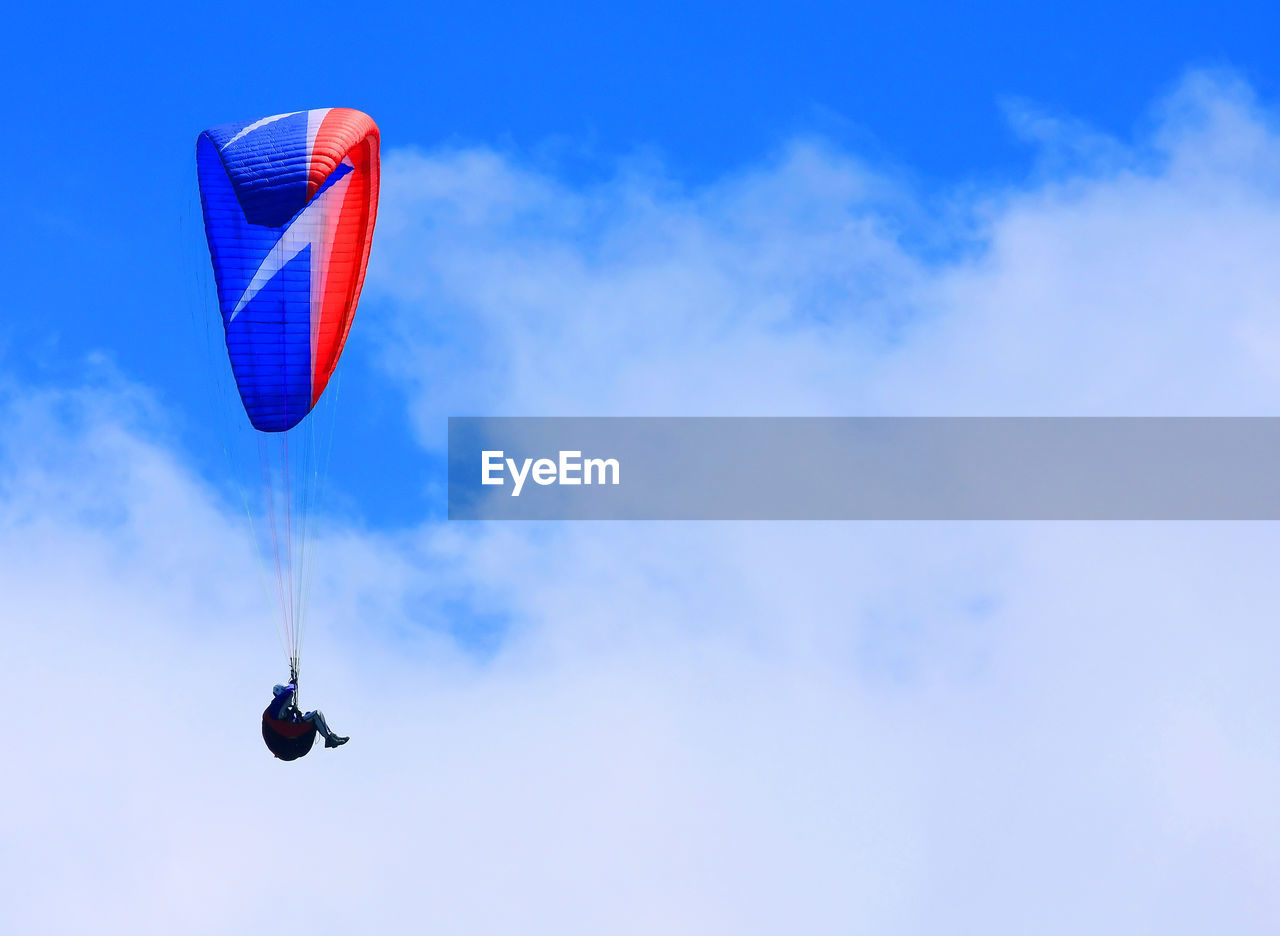 Low angle view of man paragliding in cloudy sky