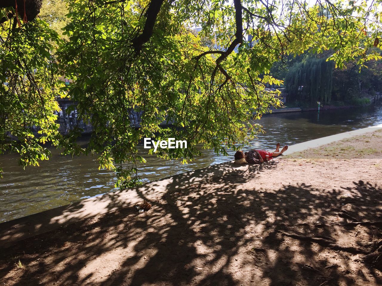 Young woman laying in shadow of trees on water