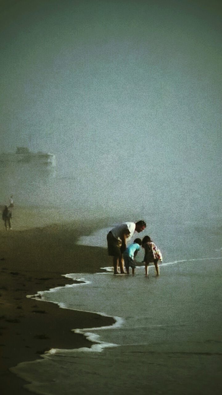 Father with children on beach against sky