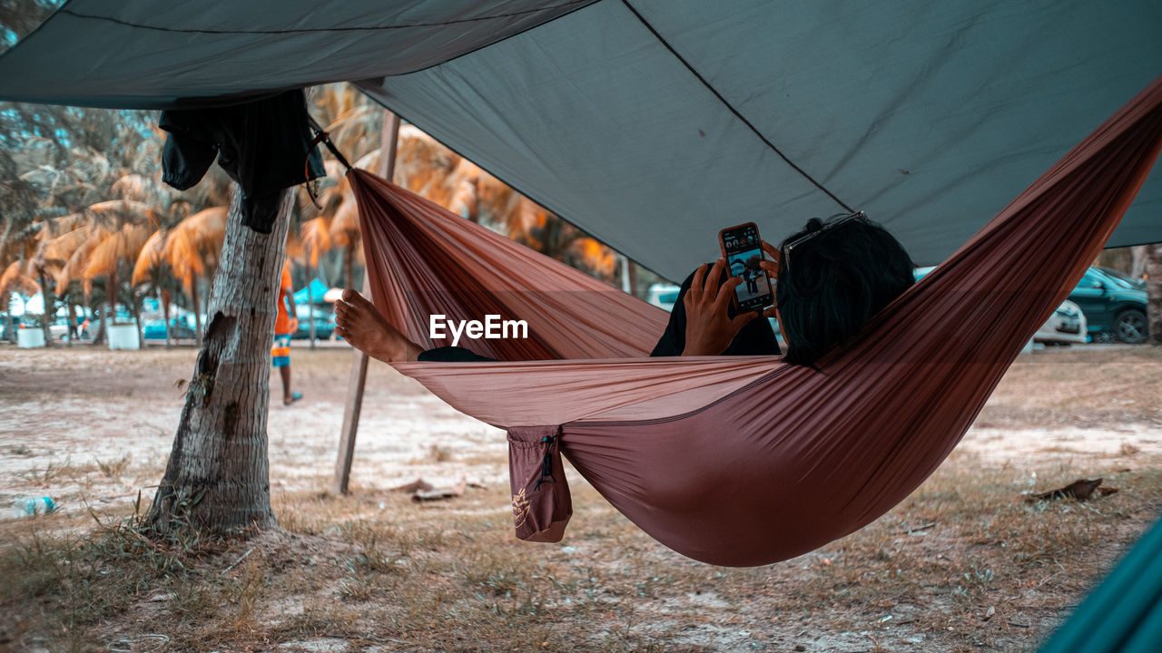 Friends using mobile phone while lying on hammock