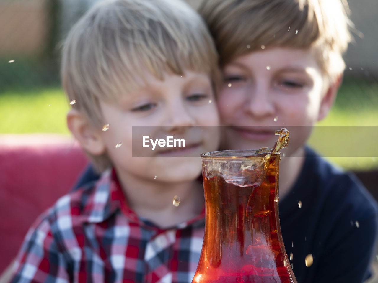 Two caucasian boys watches a splash of tea in a cup from a falling piece of sugar