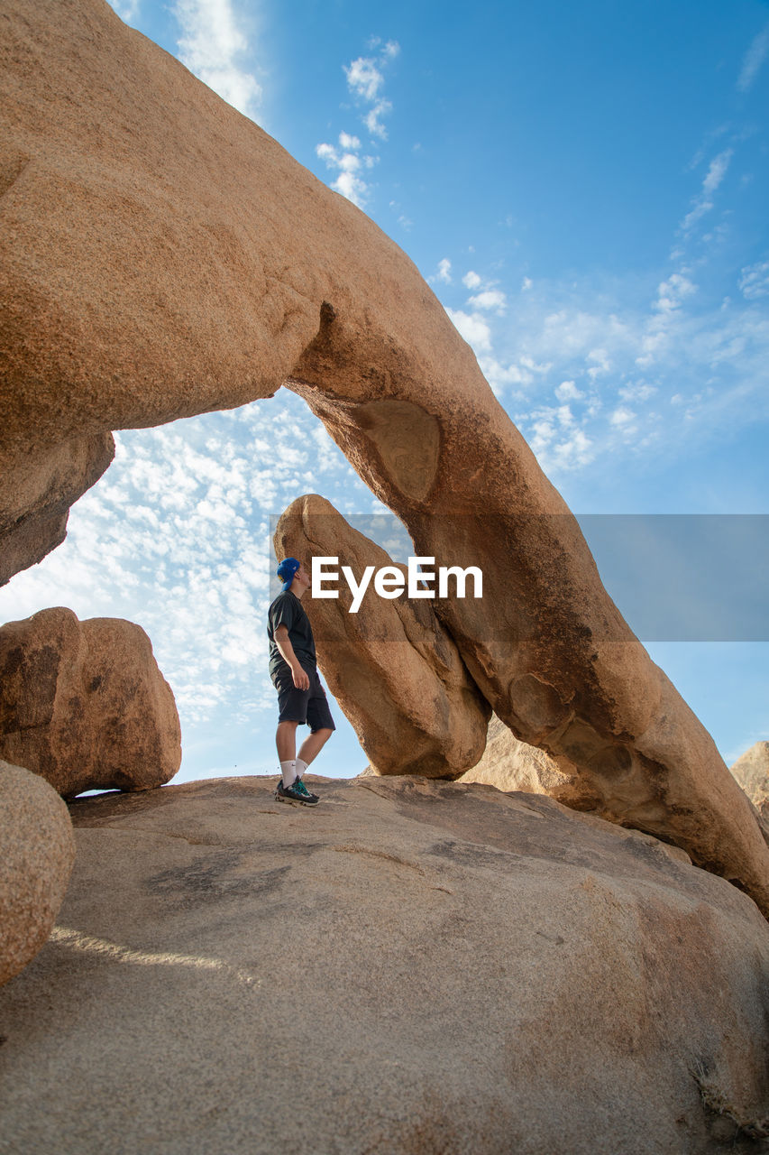 Wide angle view of man looking at arch rock in joshua tree national park against clear sky.