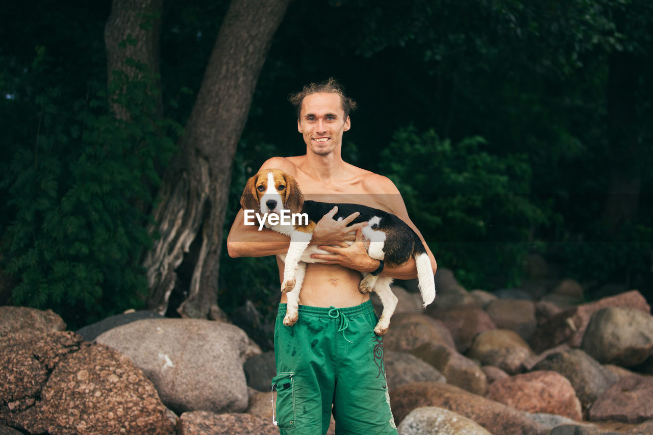 PORTRAIT OF MAN WITH DOG STANDING ON ROCK