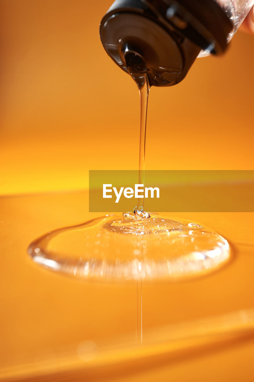 A drop of body gel or shampoo pouring from above on a yellow saturated background.