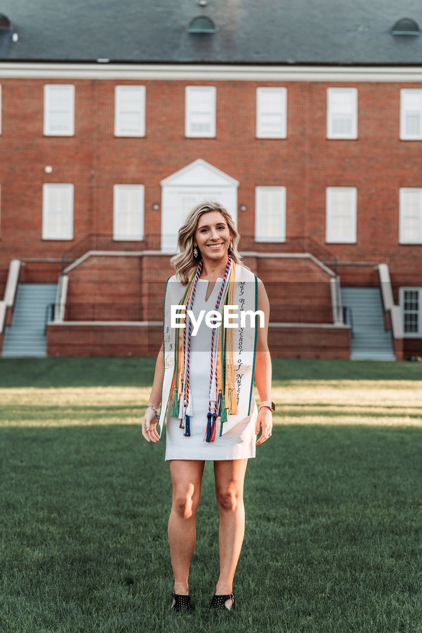 PORTRAIT OF A SMILING YOUNG WOMAN STANDING AGAINST BUILDING