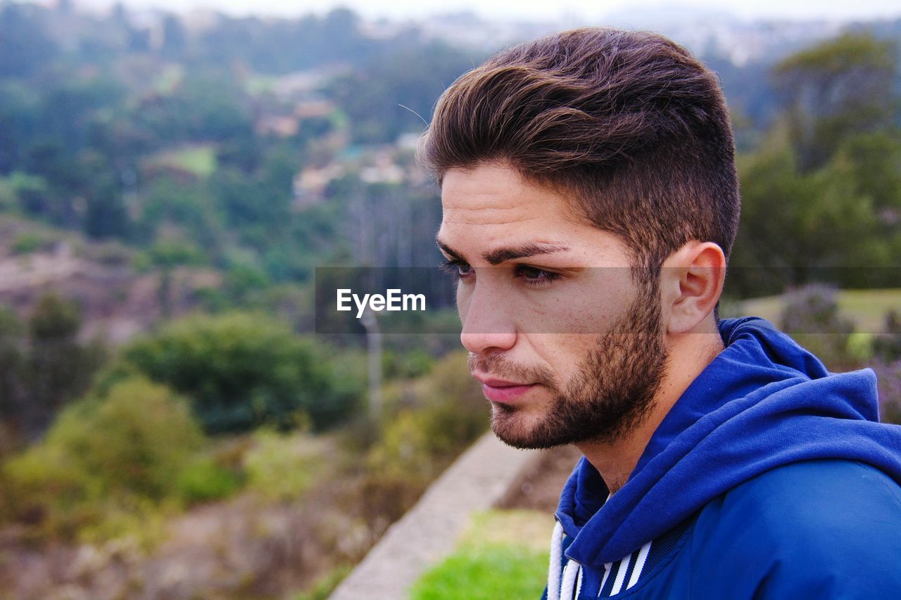 Young man looking away against trees