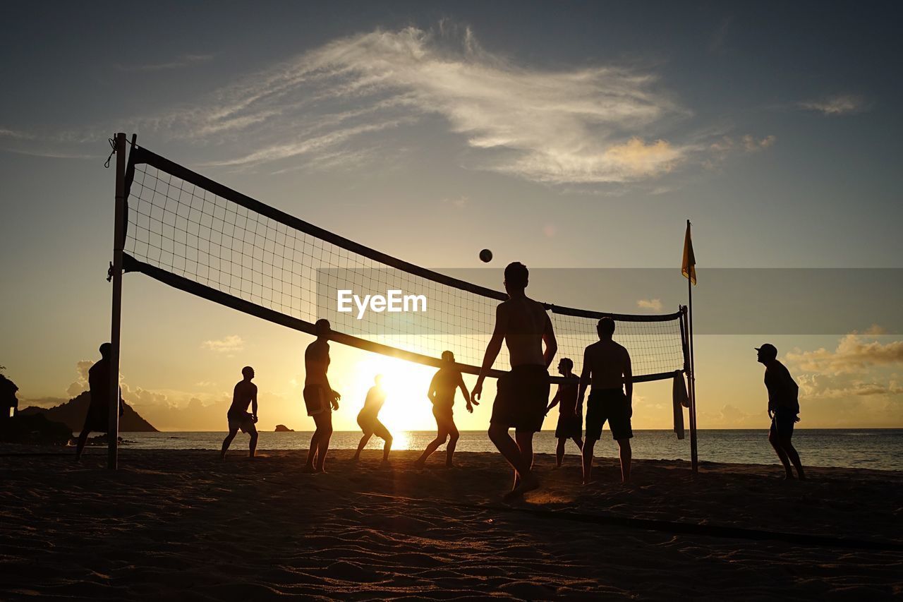 People playing volleyball at beach against sky during sunset