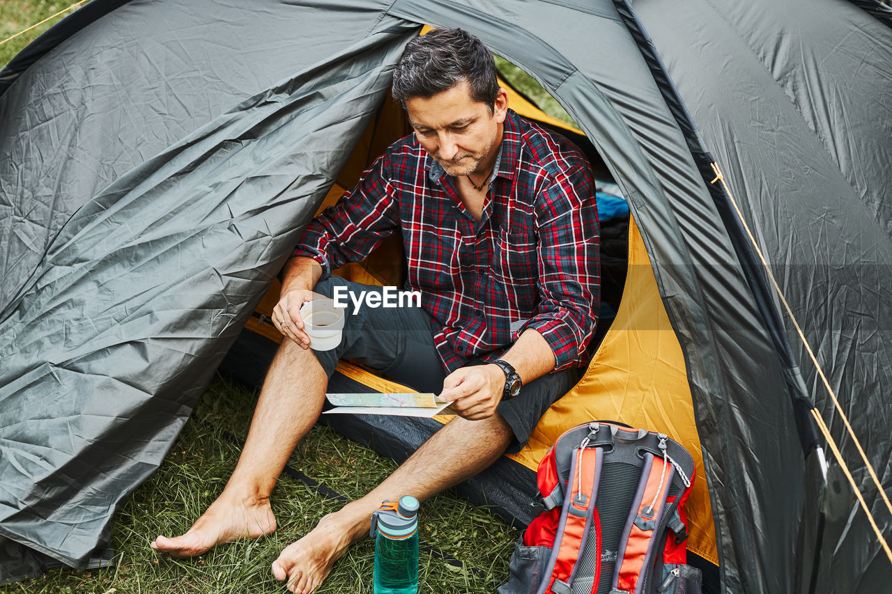 Man relaxing in tent at camping during summer vacation. planning next trip. concept of camp life