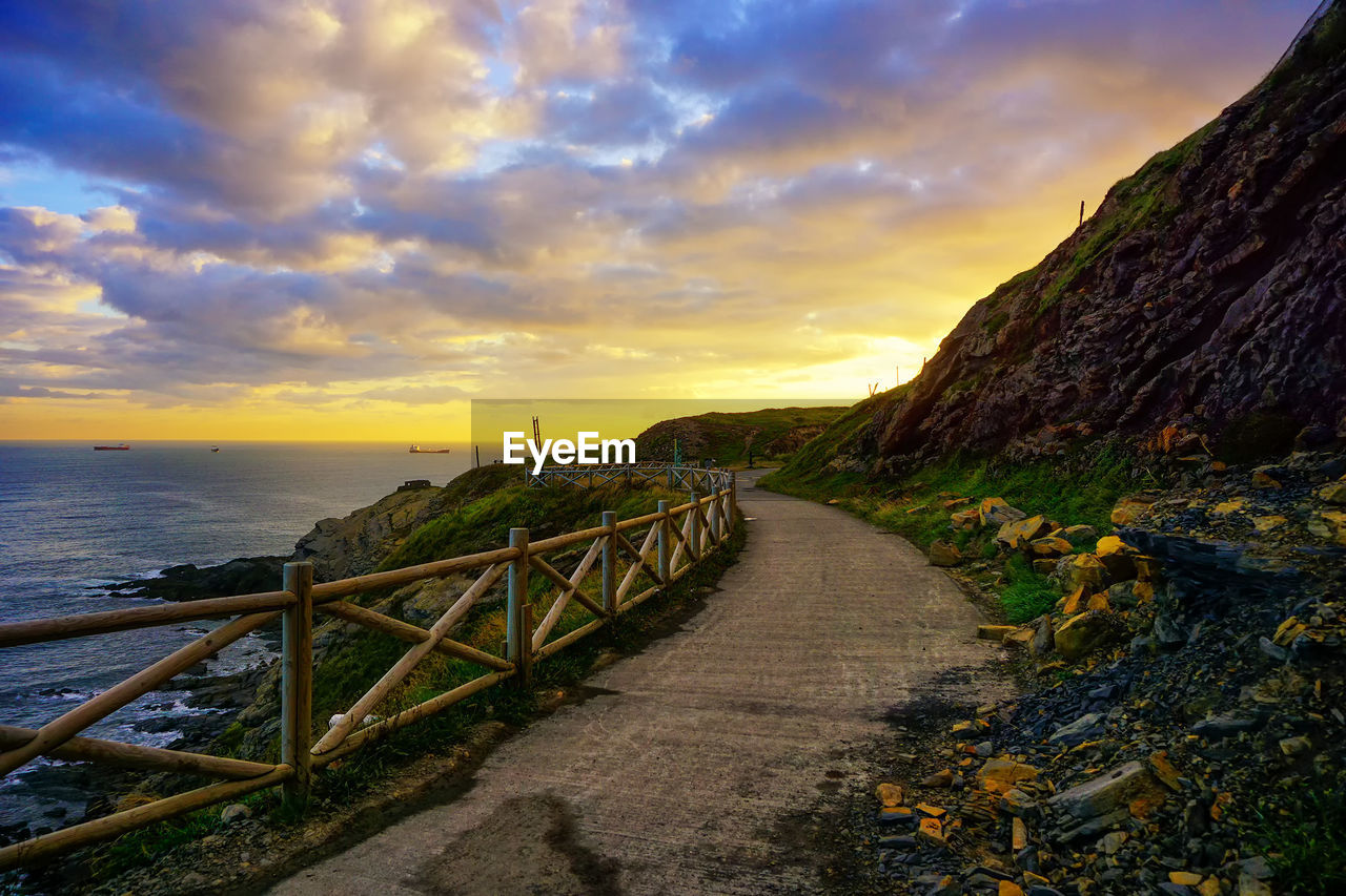 WALKWAY AMIDST SEA AGAINST SKY DURING SUNSET