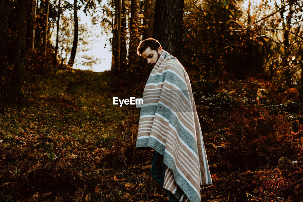 Man with shawl standing in forest during autumn