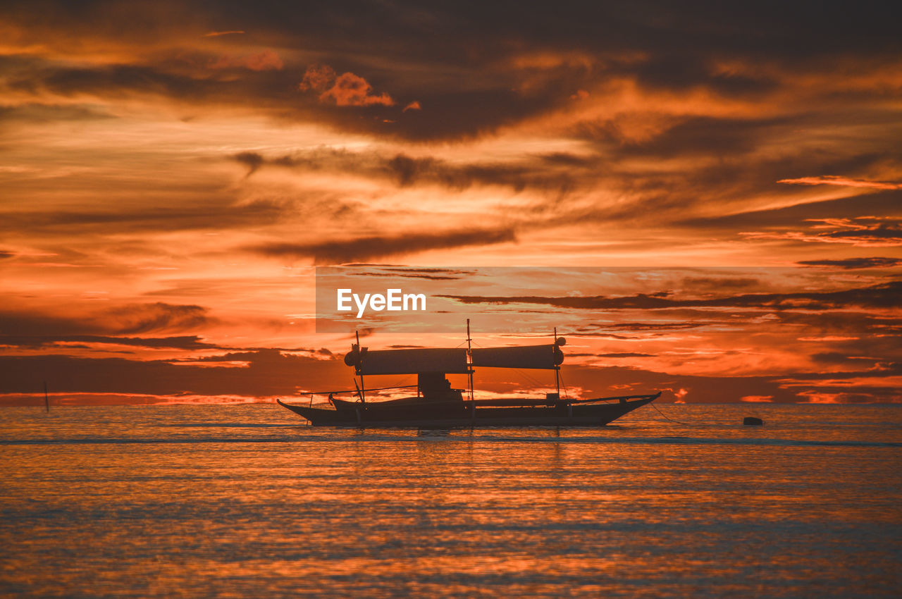 Silhouette sailboat in sea against sky during sunset