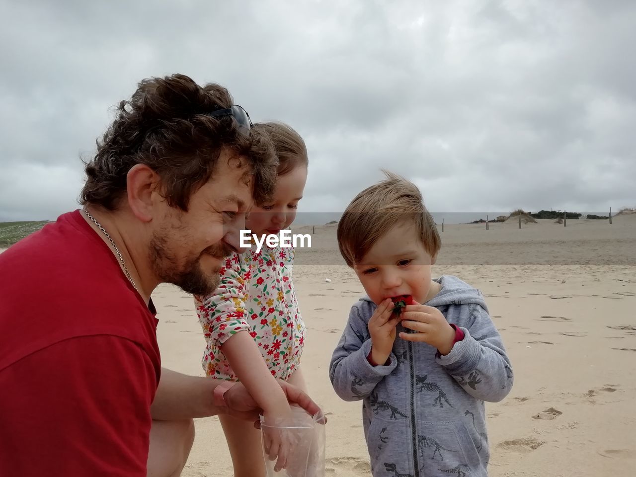 Grandpa sharing strawberries with kids on a beach.