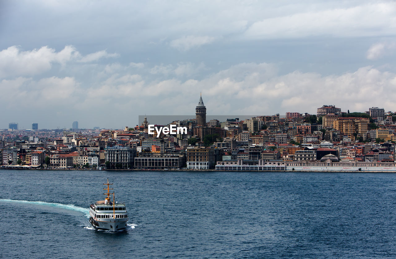 High angle view of ship sailing on strait by buildings against cloudy sky