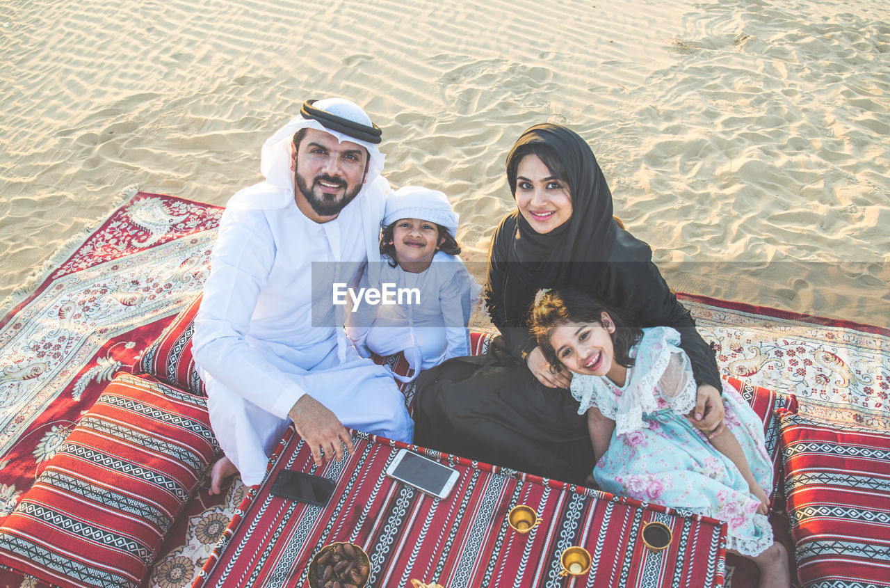 Portrait of happy family sitting on carpet at desert 