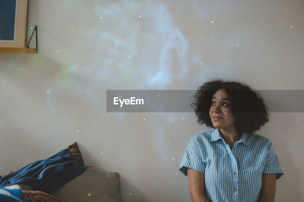 Woman looking at astro light effect falling on wall at home