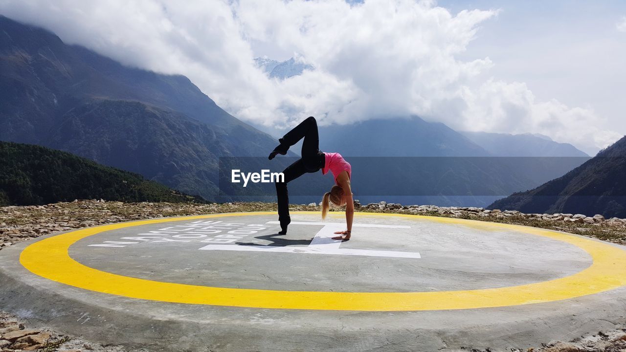 Woman doing handstand on helipad against sky