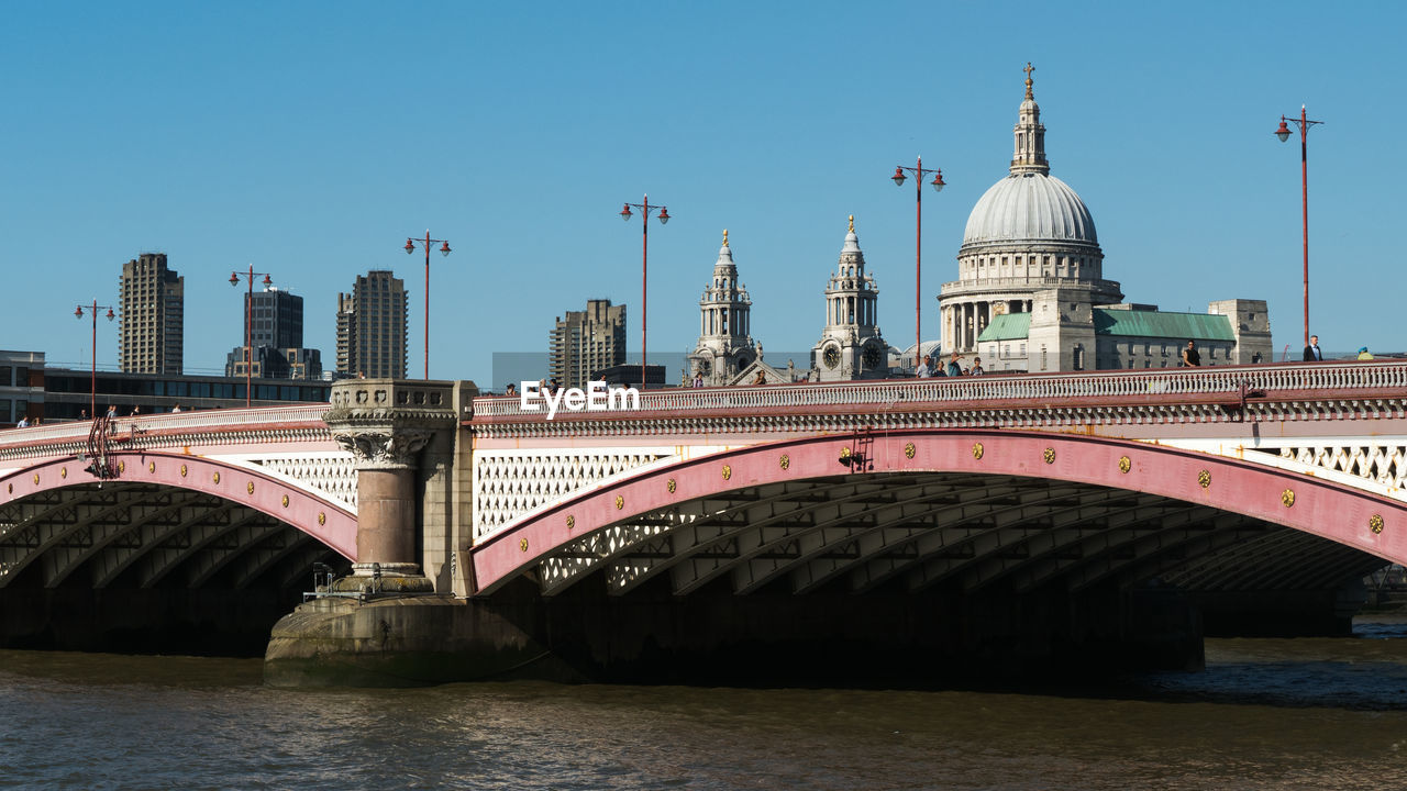 Arch bridge over river in city against clear sky