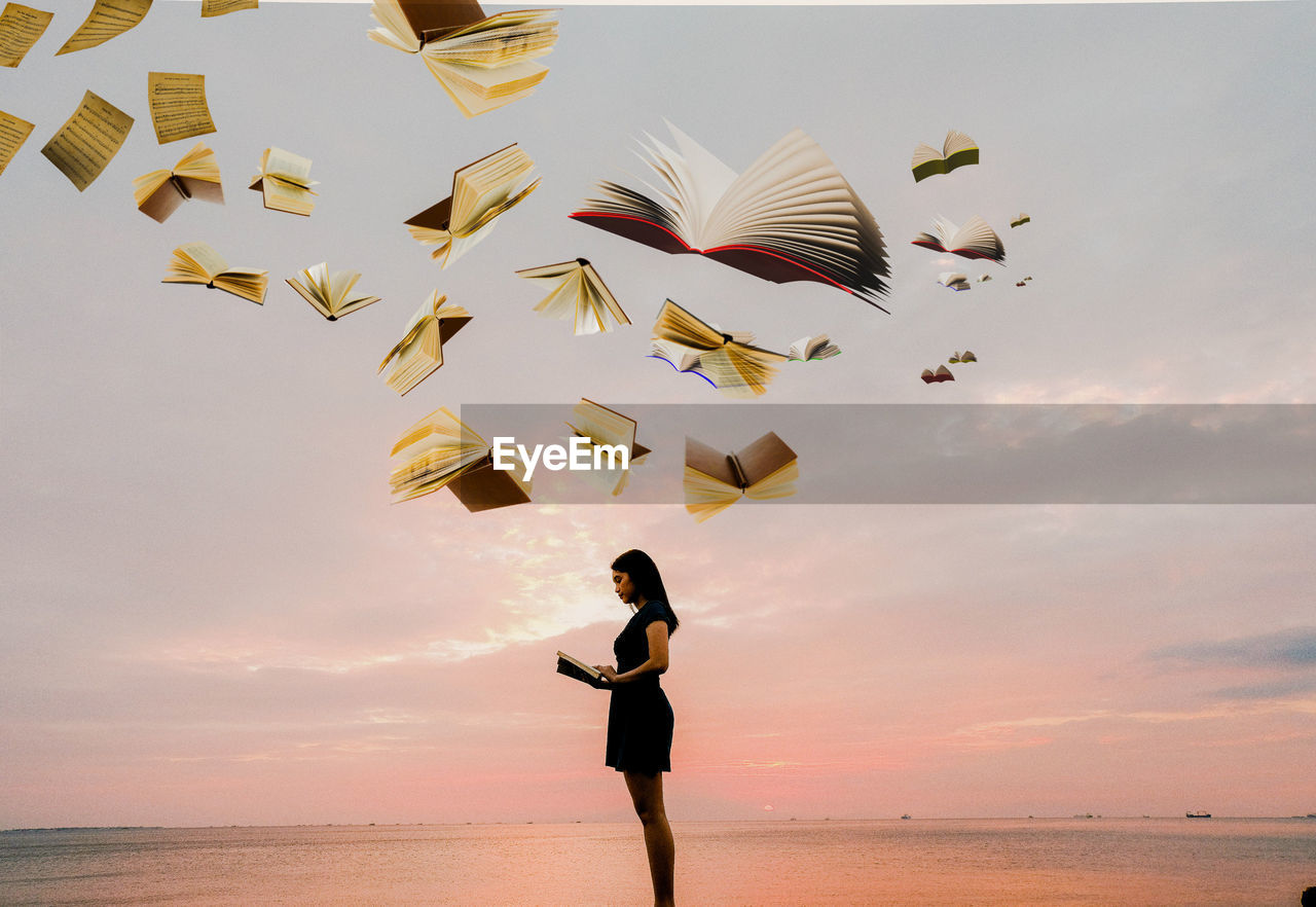 FULL LENGTH OF WOMAN FLYING OVER BEACH AGAINST SKY