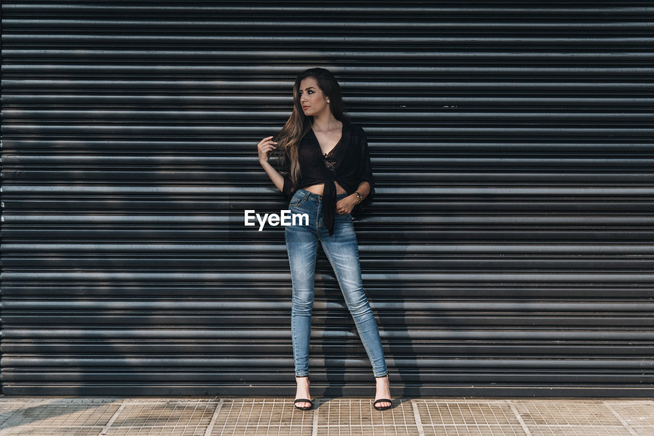 Full length of young woman standing against shutter