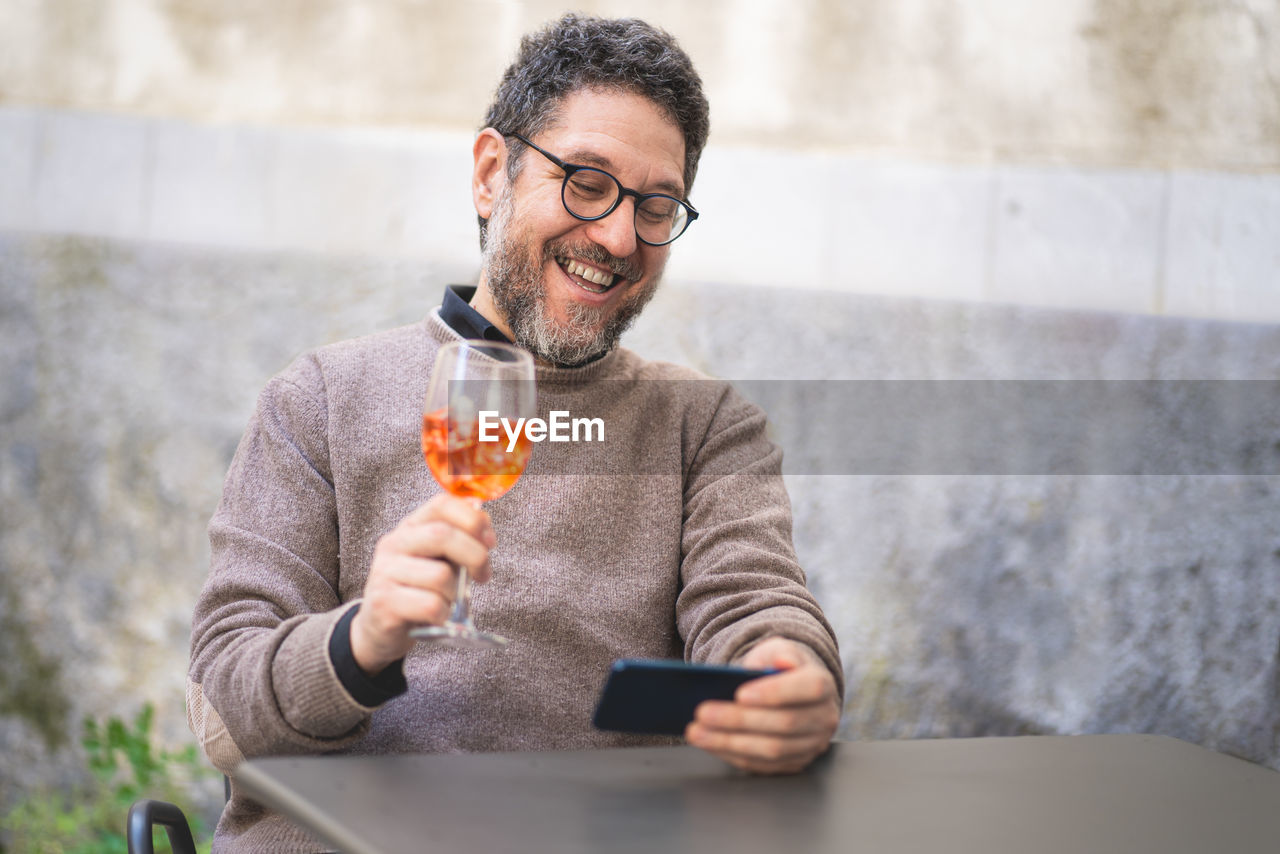 A middle-aged man toasts at a virtual party in a video call with a spritz during the quarantine