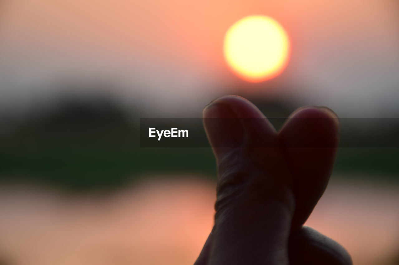 CLOSE-UP OF HAND AGAINST ORANGE SKY