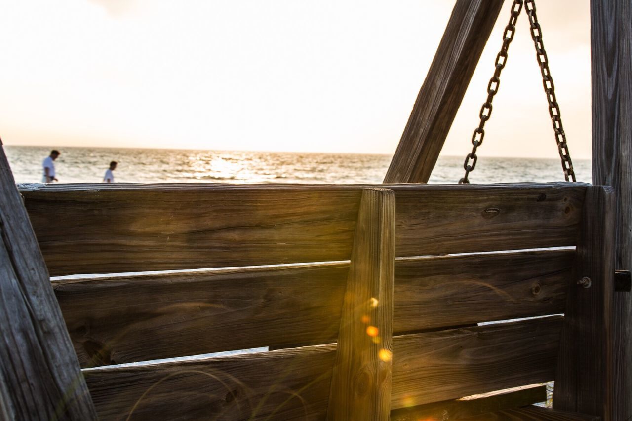 Close-up of wooden bench at beach during sunset