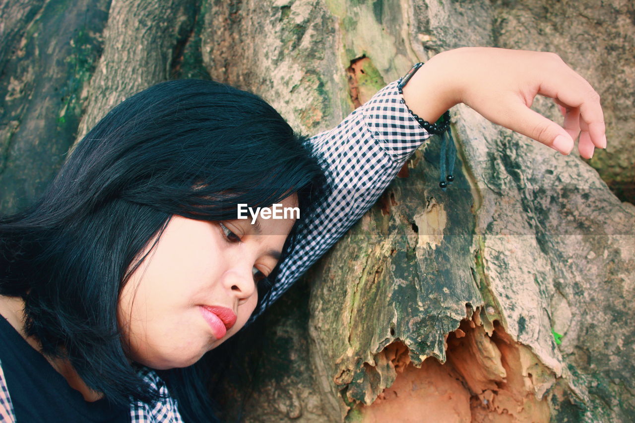Beautiful young woman looking down by tree trunk