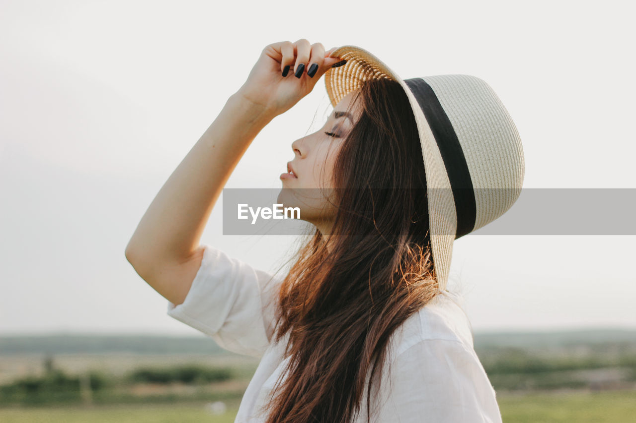 Woman wearing hat while standing on grass against sky