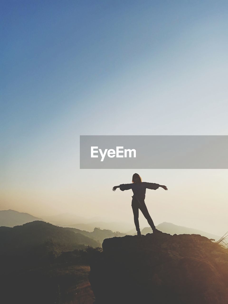 Silhouette woman with arms outstretched standing on mountain against clear sky