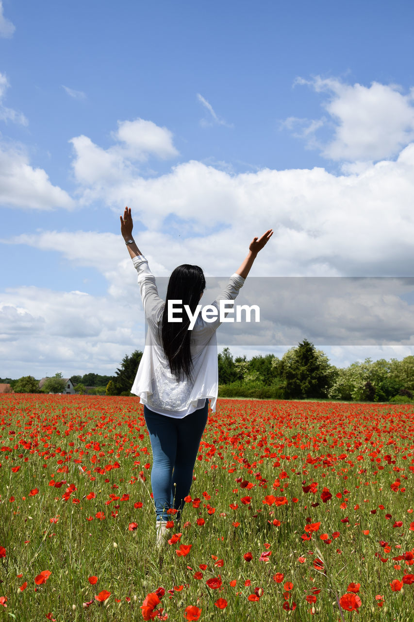 Rear view of woman with arms raised standing on flowerbed