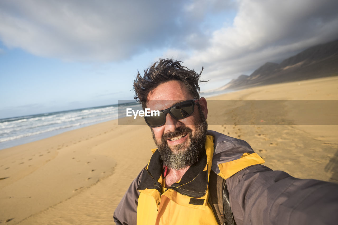 Portrait of man wearing sunglasses at beach against sky