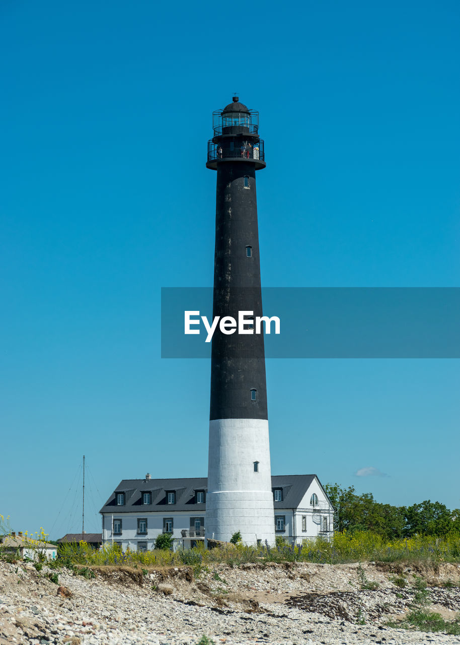 Low angle view of lighthouse by building against clear blue sky