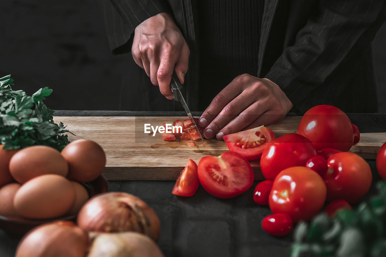 Midsection of person cutting tomato on wooden cutting board against black background