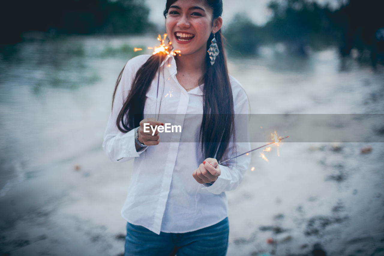 Portrait of teenage girl holding sparkler while standing outdoors