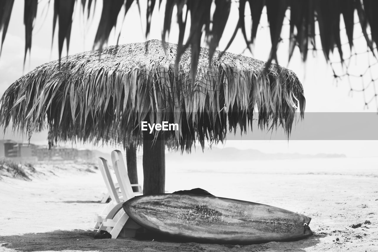 Boat moored by lounge chair under thatched roof at beach