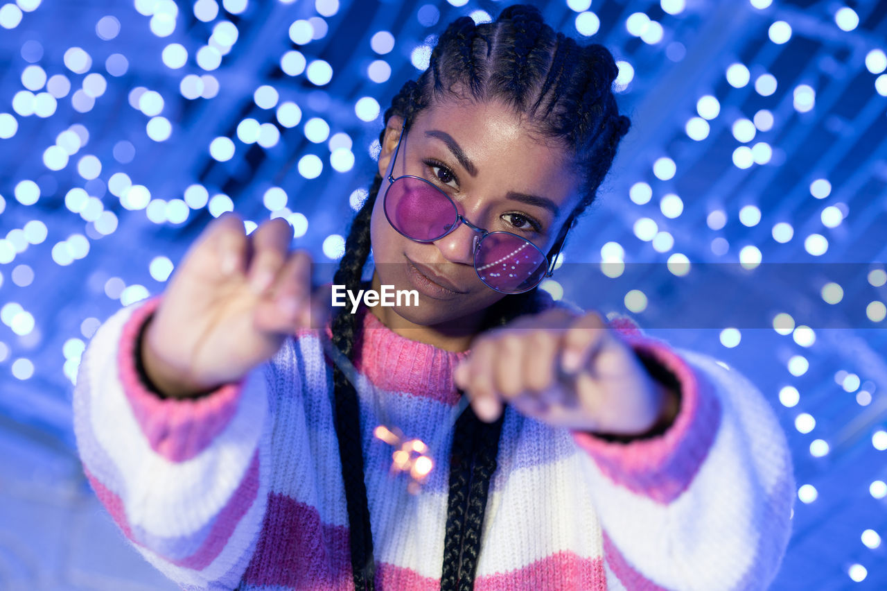 Cheerful black woman with braided hairstyle and pink glasses enjoying christmas lights