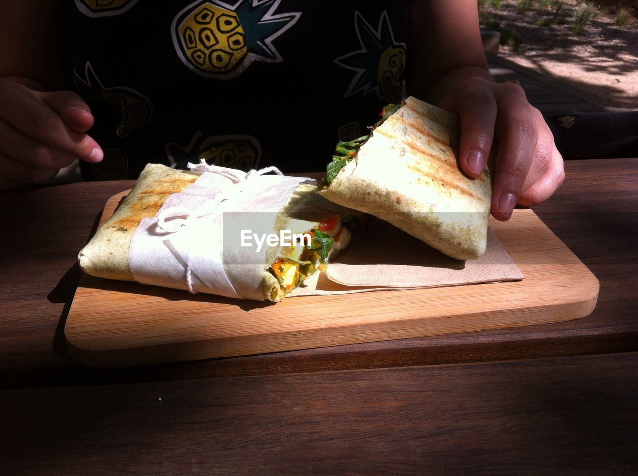 Midsection of person holding wrap sandwich on serving board