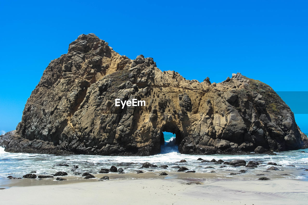 Scenic view of beach and rock formation in sea against clear blue sky
