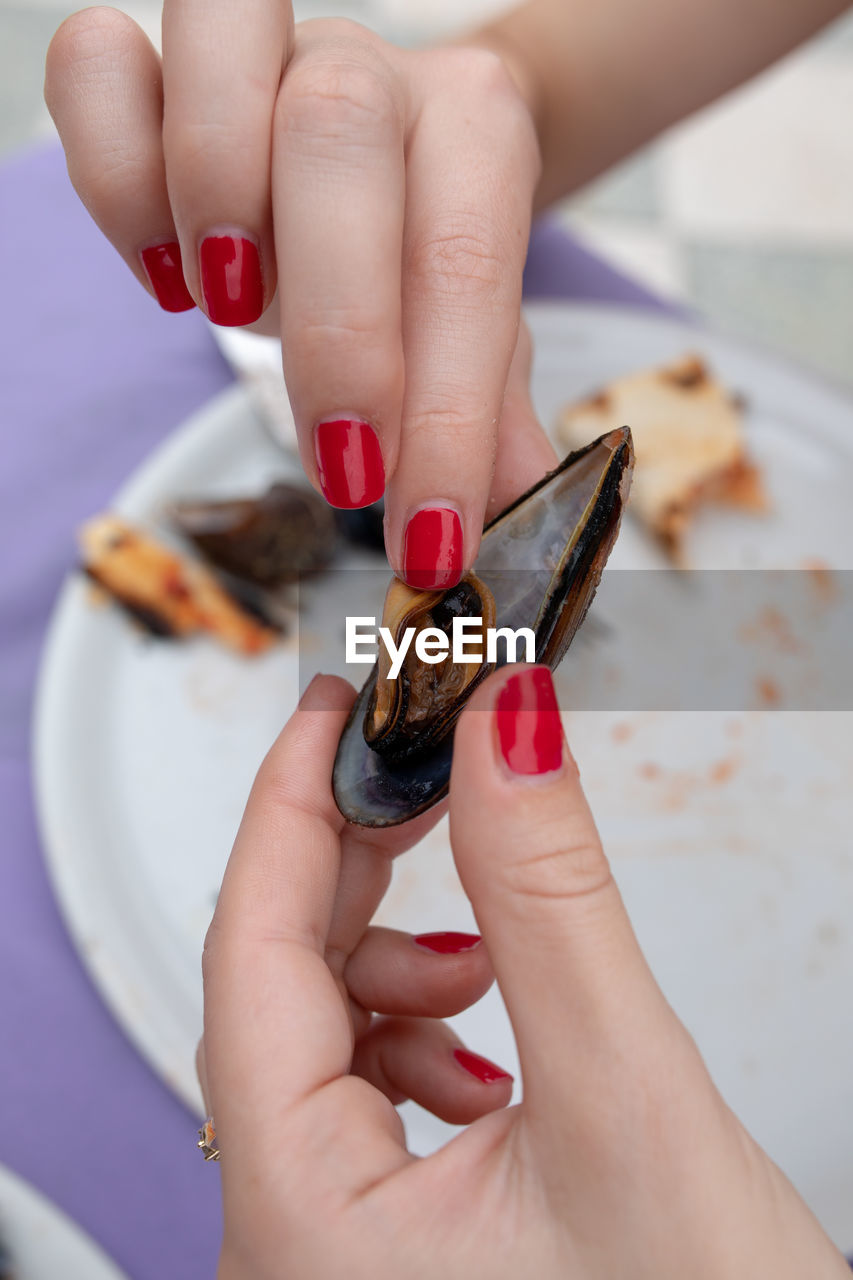 Woman with red nail polish holding mussel over plate at table