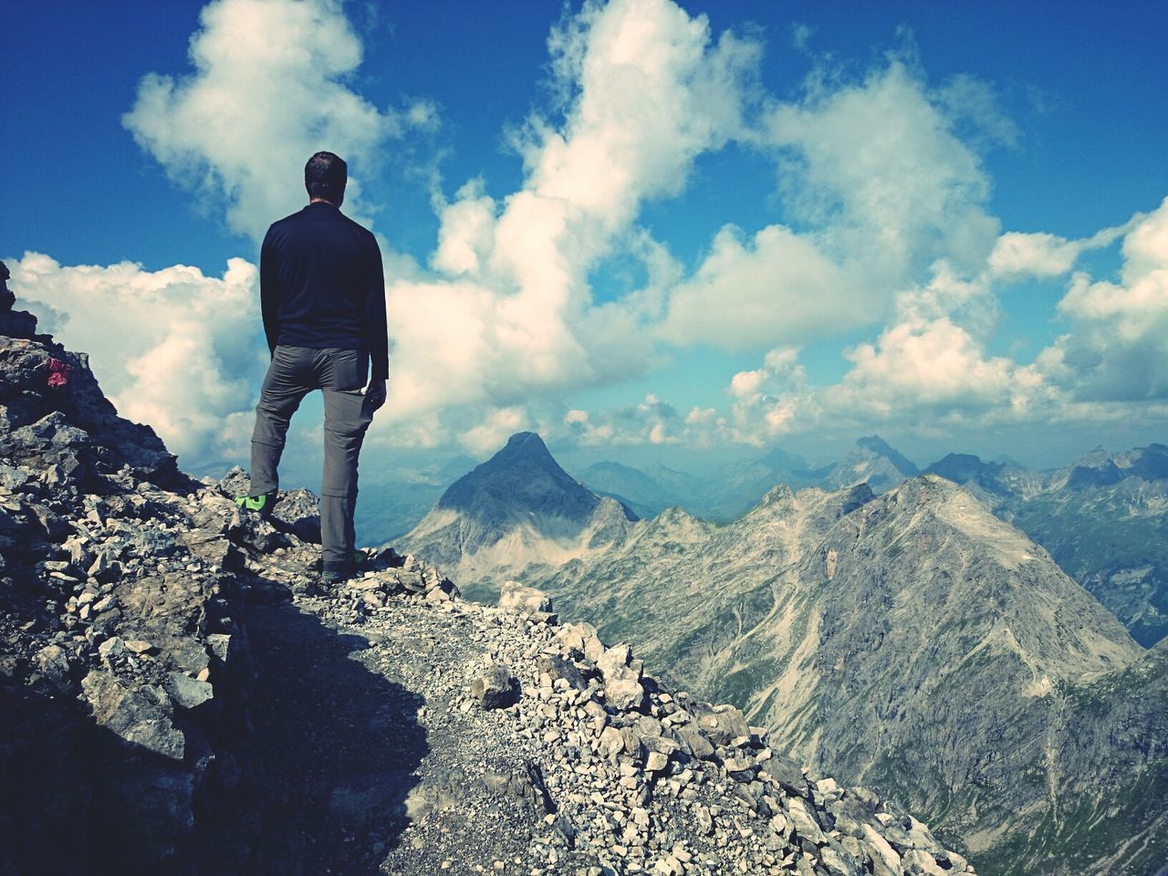 Rear view of man standing on mountains against cloudy sky