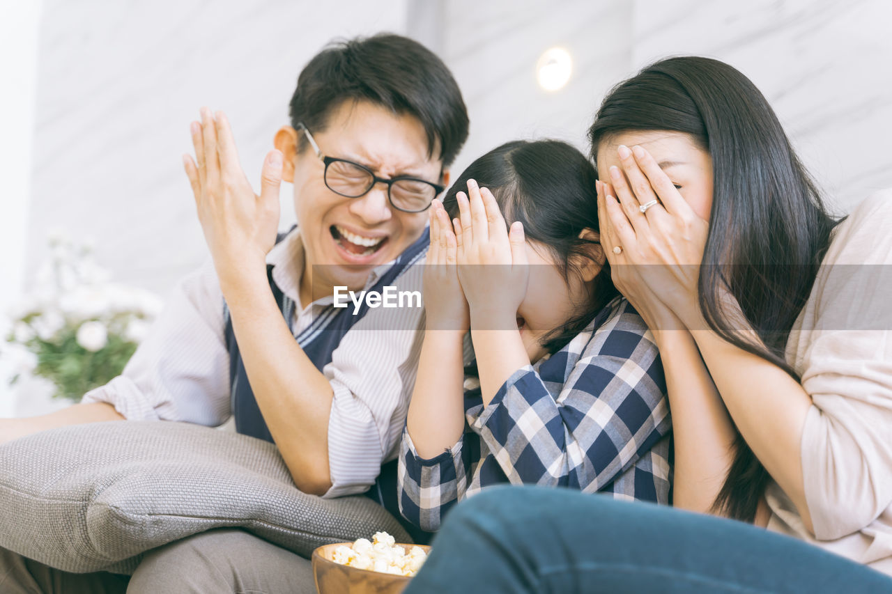 Smiling parents with daughter covering faces in living room at home